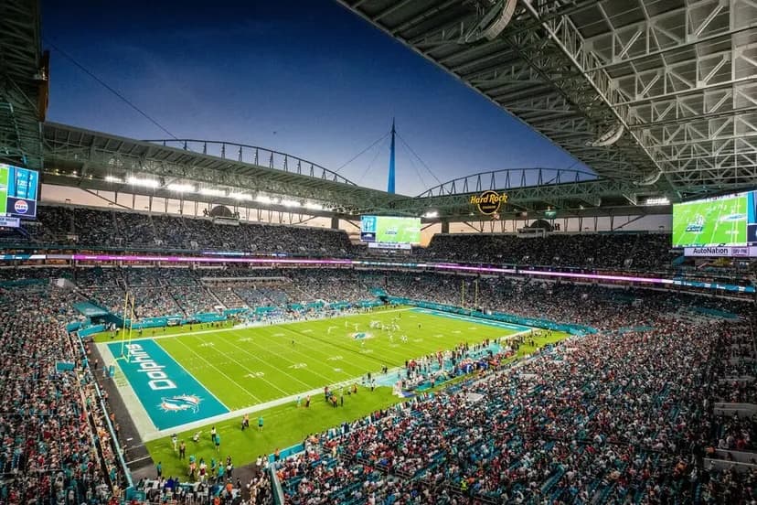 A packed Hard Rock Stadium at dusk during a Miami Dolphins game, the Hard Rock sign above the open end of the bowl